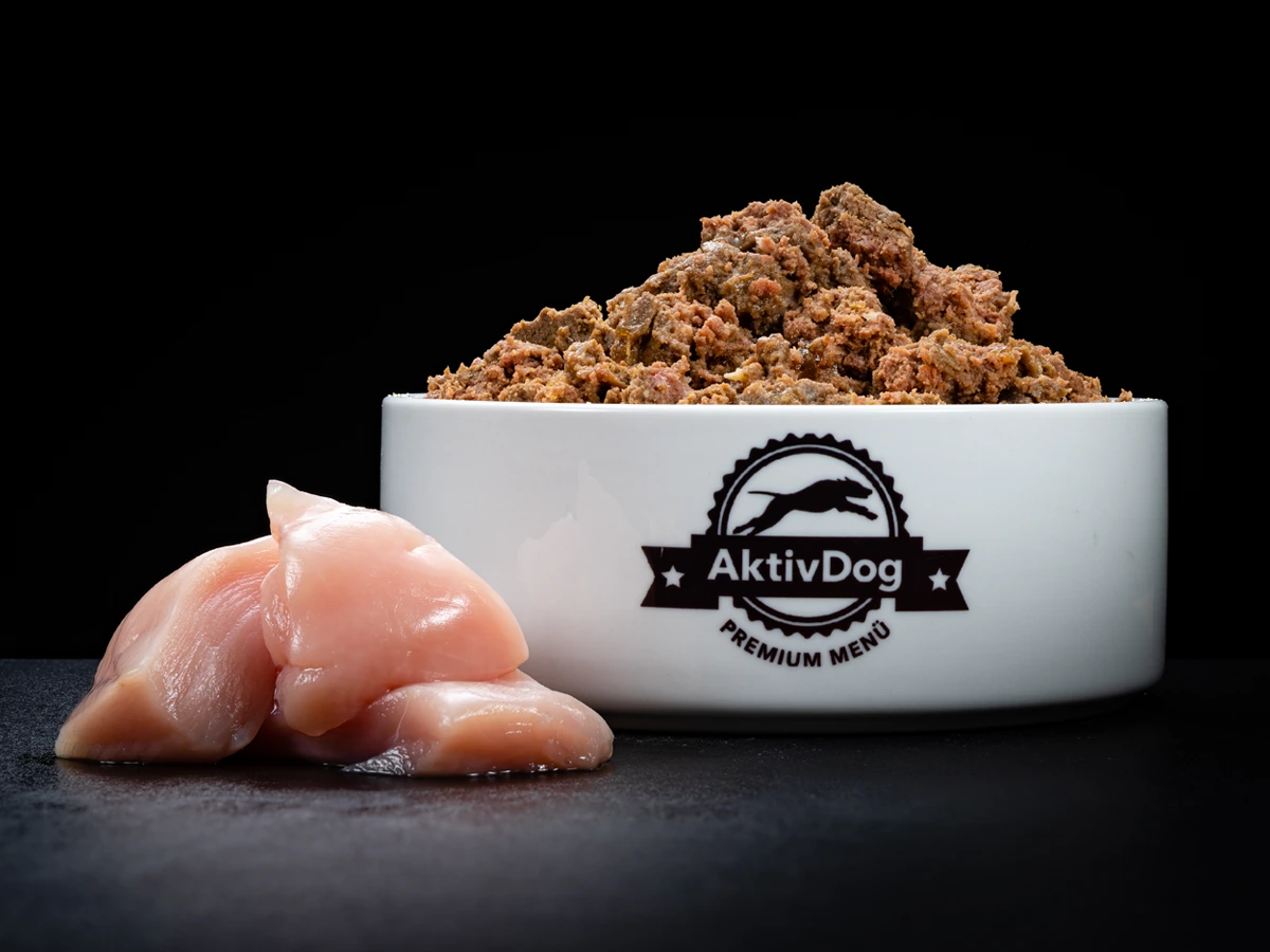 Großaufnahme von AktivDog 100% Hundefutter Huhn mit links daneben liegendem aufgeschnittenen rohen Schweizer Poulet